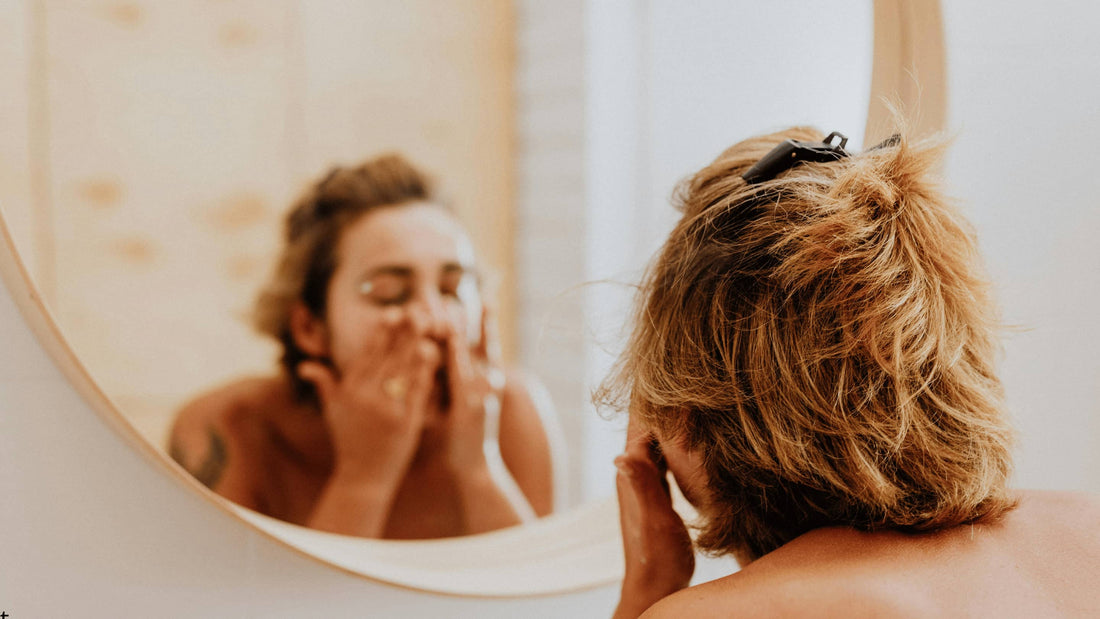 Person som tvättar ansiktet framför spegeln, illustrerar rengöring av huden efter microneedling-behandling.